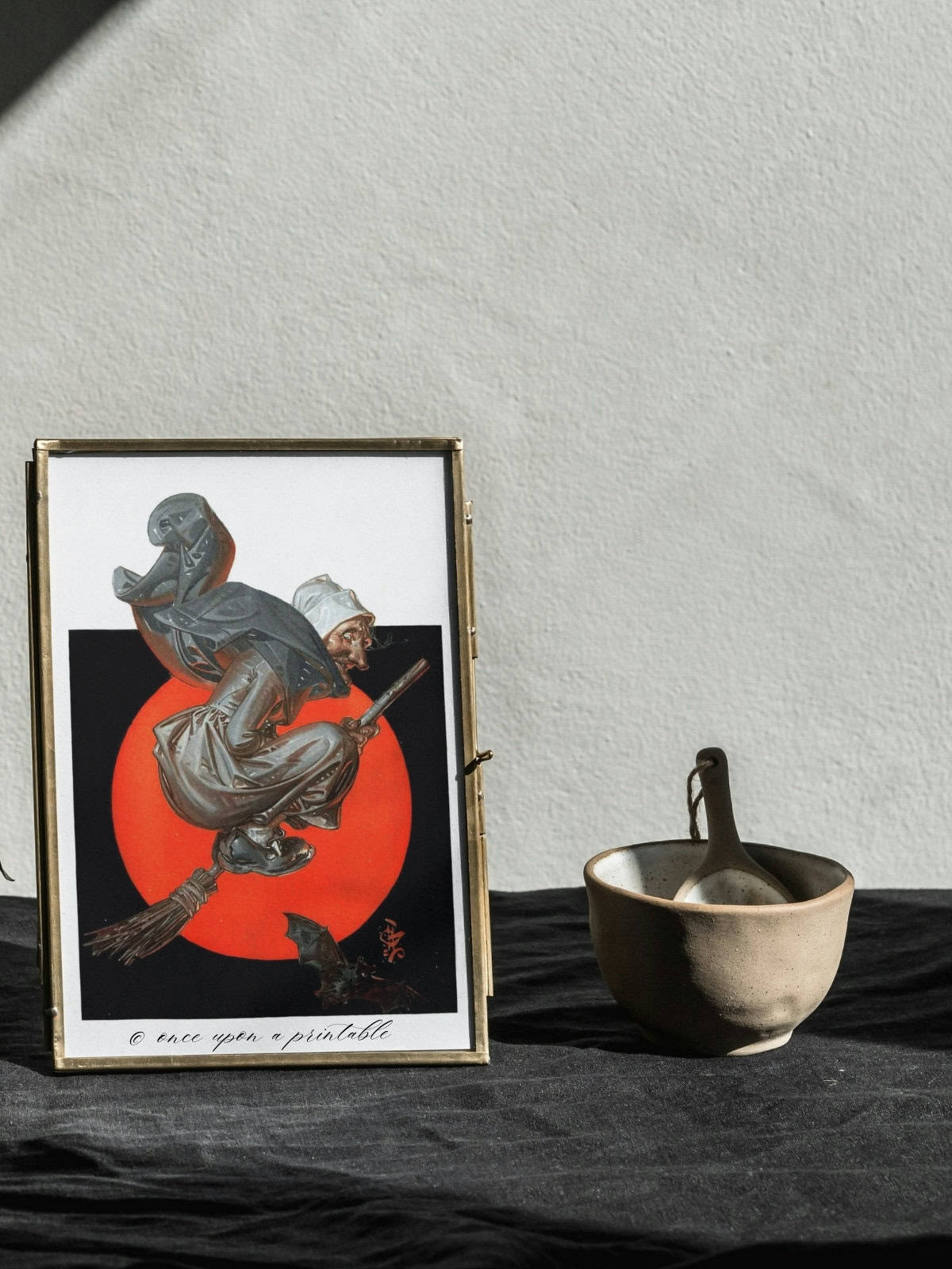 A vintage illustration of a witch flying on a broomstick framed and displayed next to a mortar and pestle.