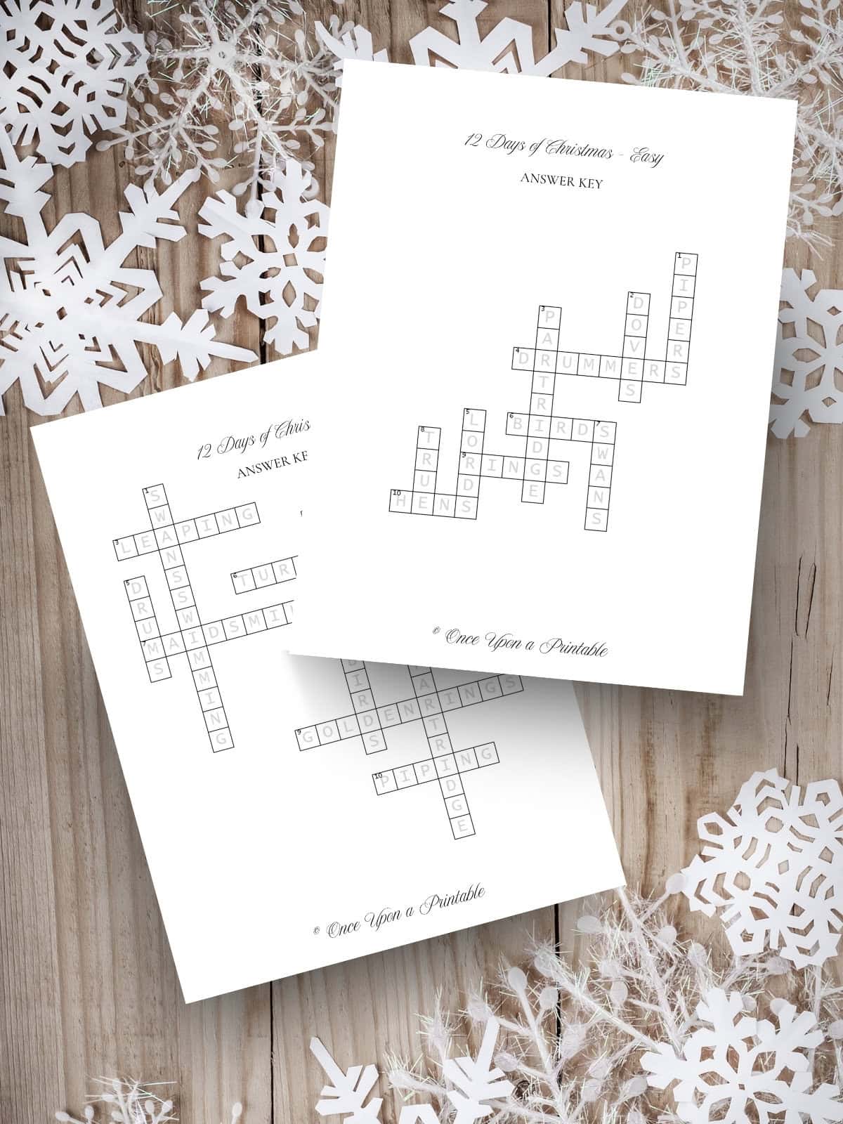 12 Days of Christmas crossword puzzle answer keys laying on a wooden background with paper snowflakes.