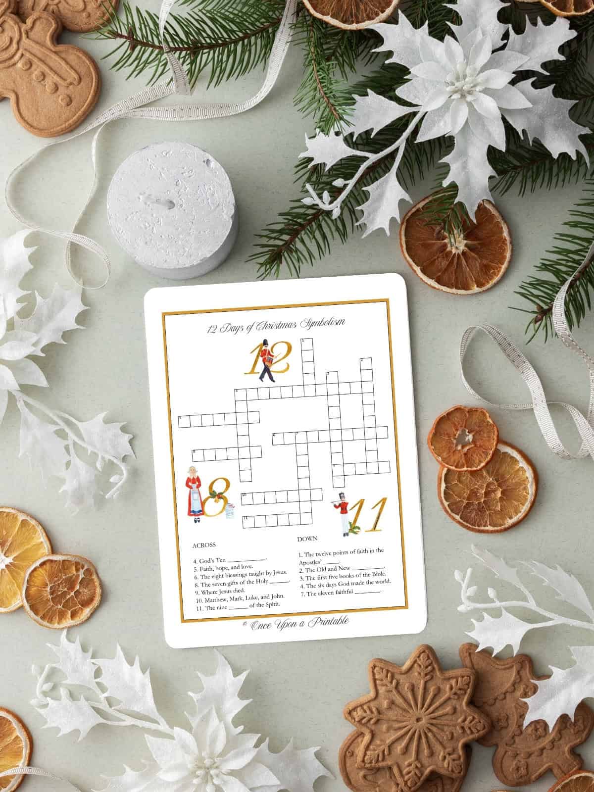 The 12 days of christmas illustrated crossword puzzle with symbolism clues laying on a table with dried oranges, garland, and paper snowflakes.