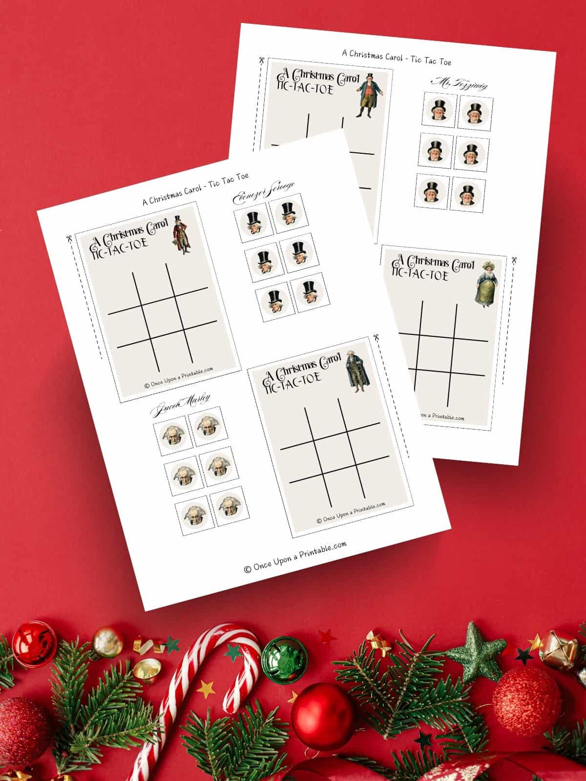 A Charles Dickens inspired A christmas carol illustrated tic tac toe cards with tokens printables laying on a red background with garland, candy, and ornaments.