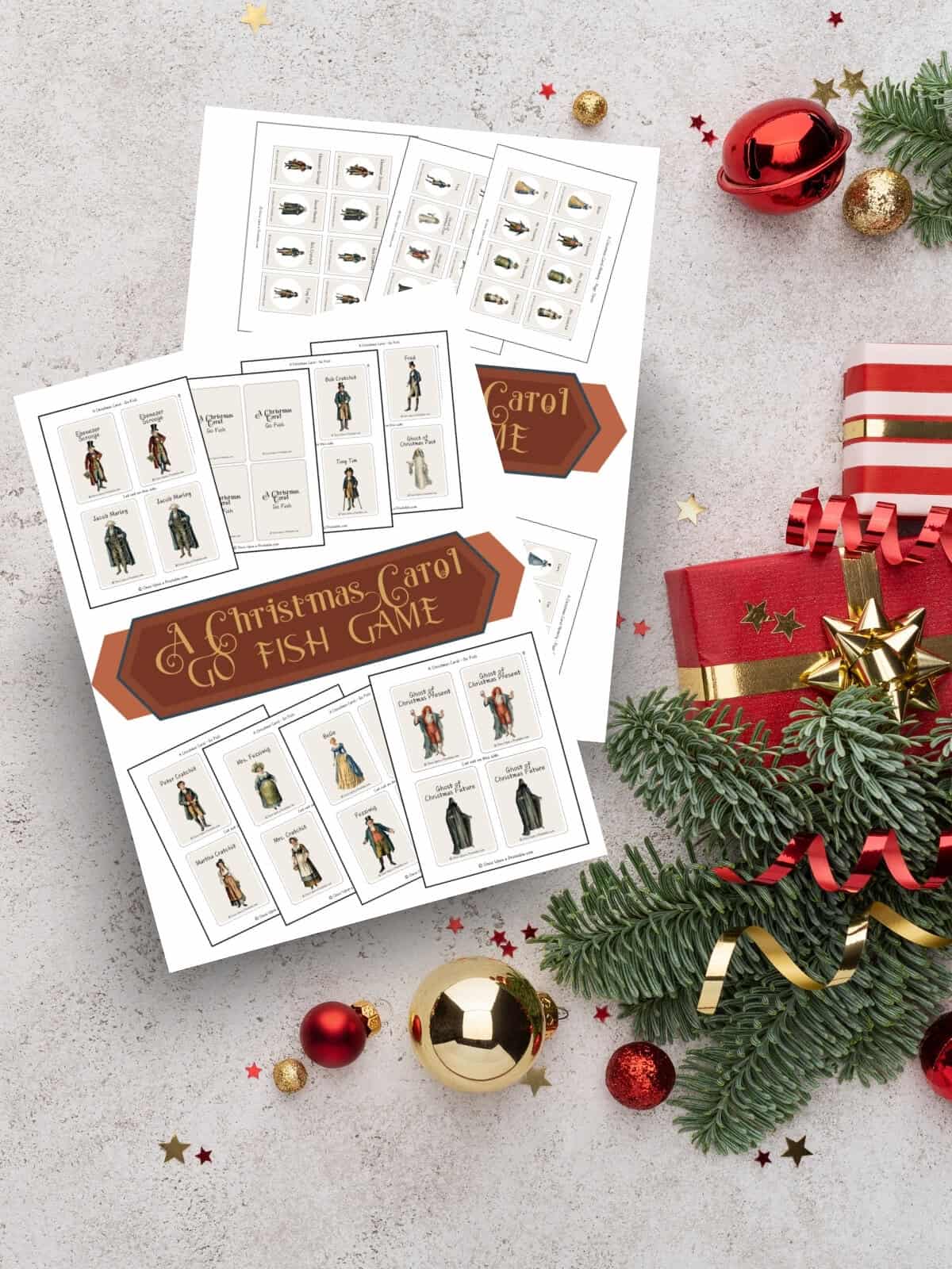 A Christmas Carol themed printables with original graphic art laying on a grey background with garland and christmas tree ornaments.