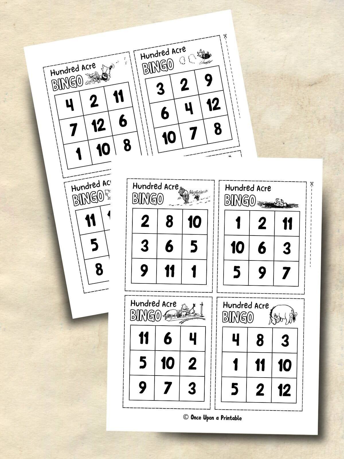 Hundred Acre wood bingo card game printables with original illustrations by E. H. Shepard laying on a brown surface.