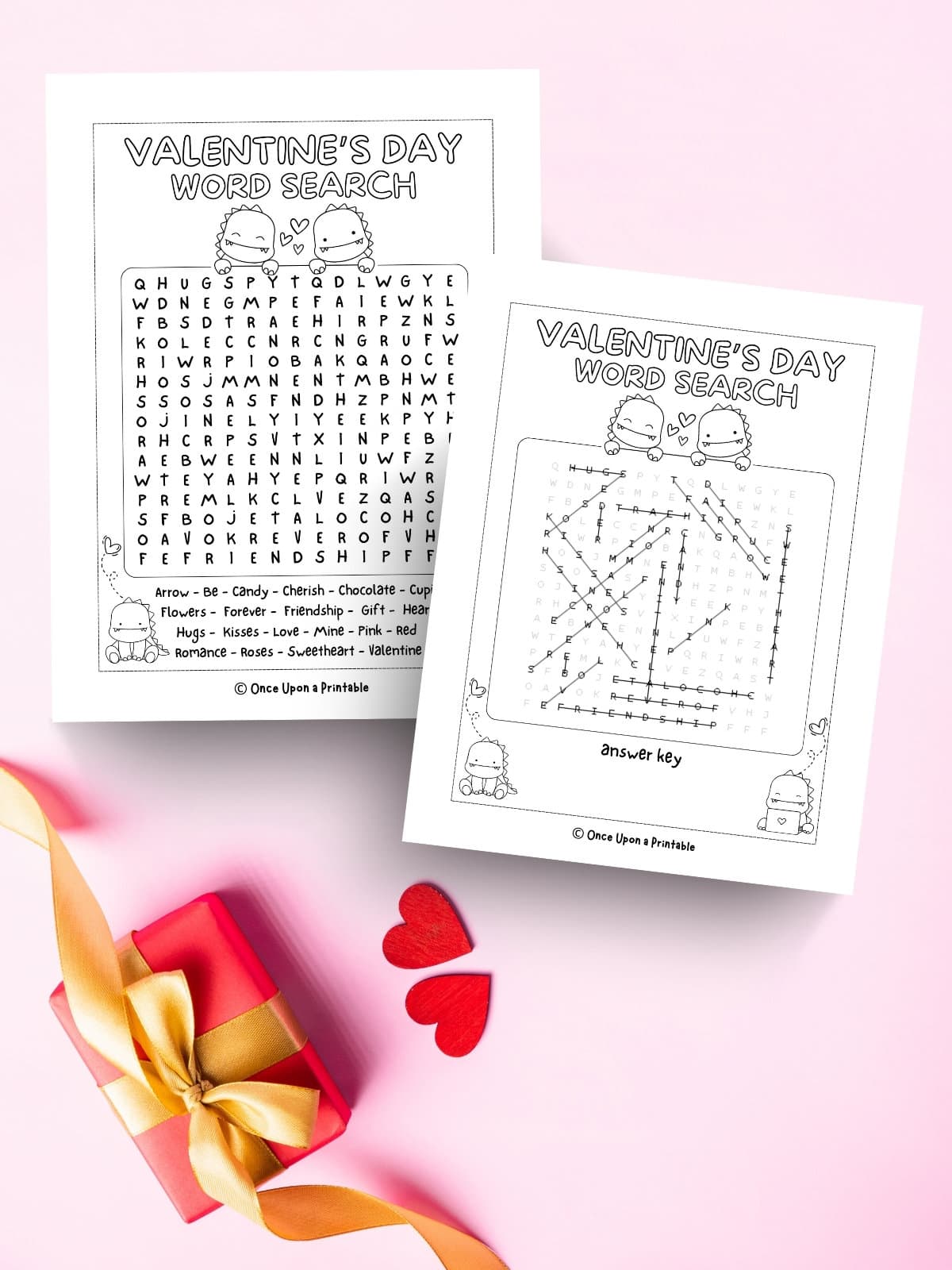 Dinosaur themed Valentine's Day crossword puzzle and answer key printed and laying on a pink background with a box.