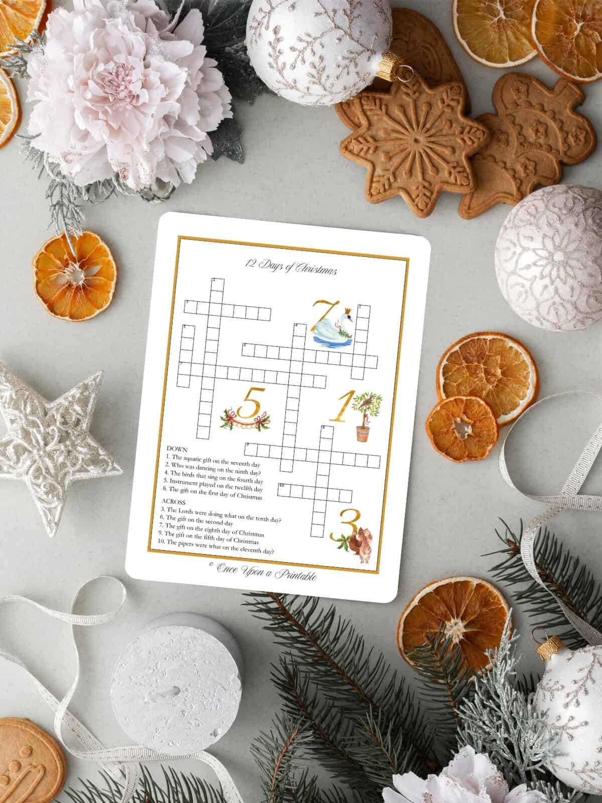 The 12 days of christmas illustrated crossword puzzle with symbolism clues laying on a table with dried oranges, garland, and paper snowflakes.