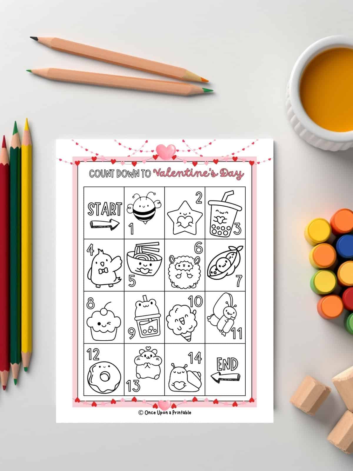 Coloring countdown calendar for Valentine's day with cute little graphics to color in, next to coloring pencils and paints.