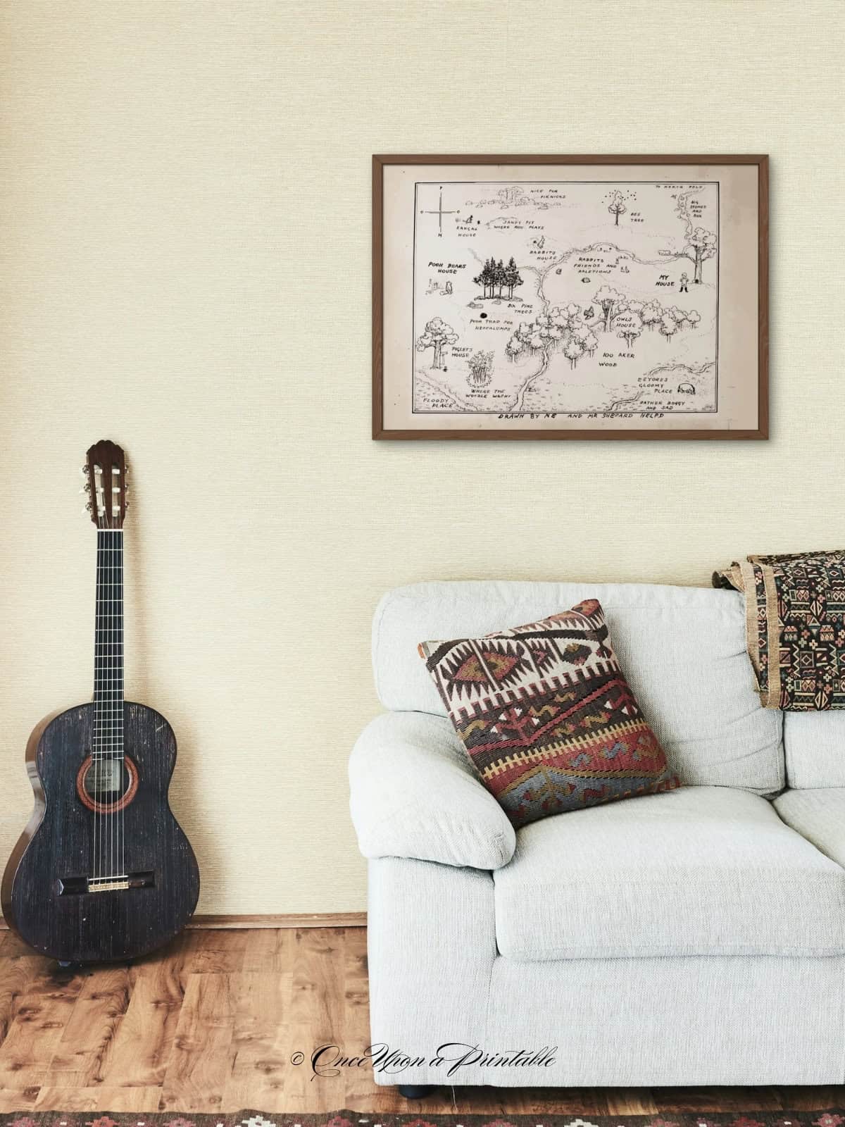 Classic hundred acre wood map framed and sitting above a couch and guitar. 