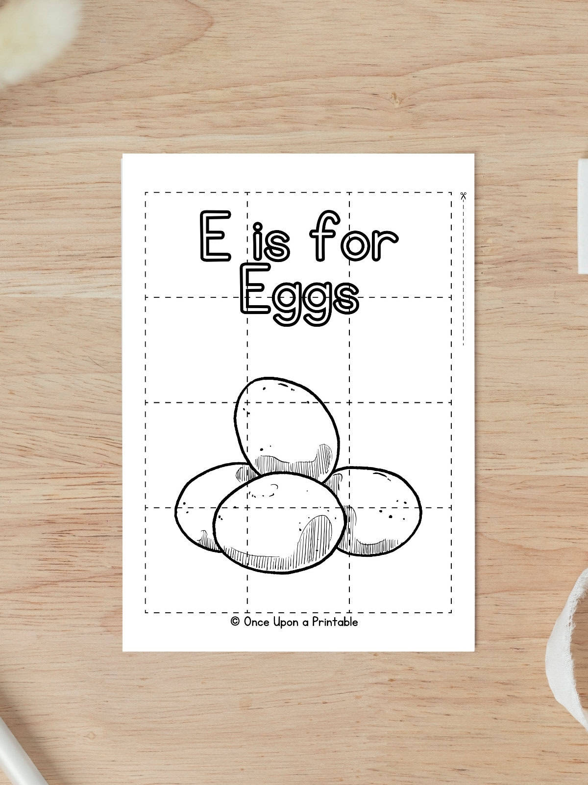 E is for Eggs coloring puzzle activity worksheet laying on a wooden table.