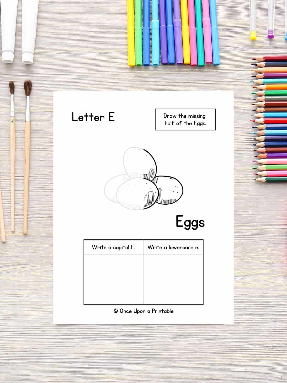 Finish the eggs drawing and letter practice page laying on a table with coloring pencils and paint brushes.