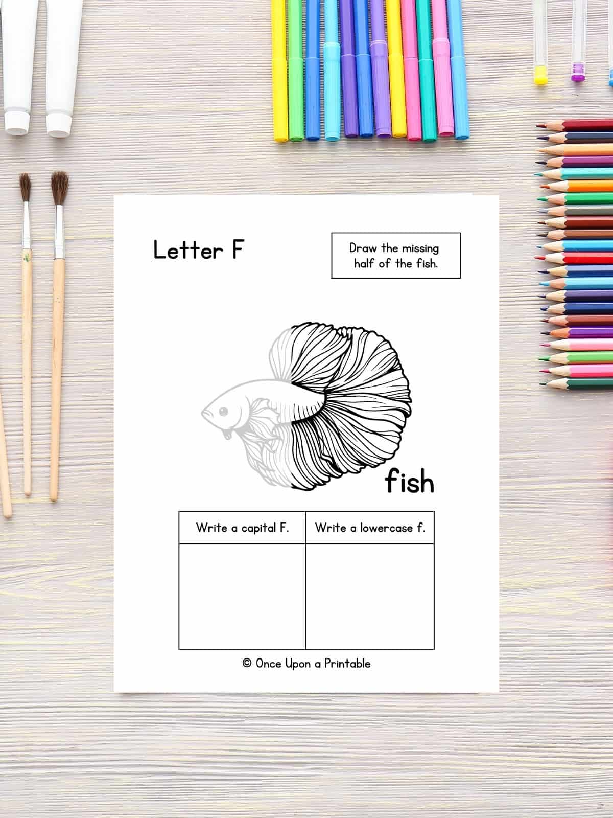 Finish the drawing, F is for Fish with a beta fish graphic laying on a table with colored pencils.