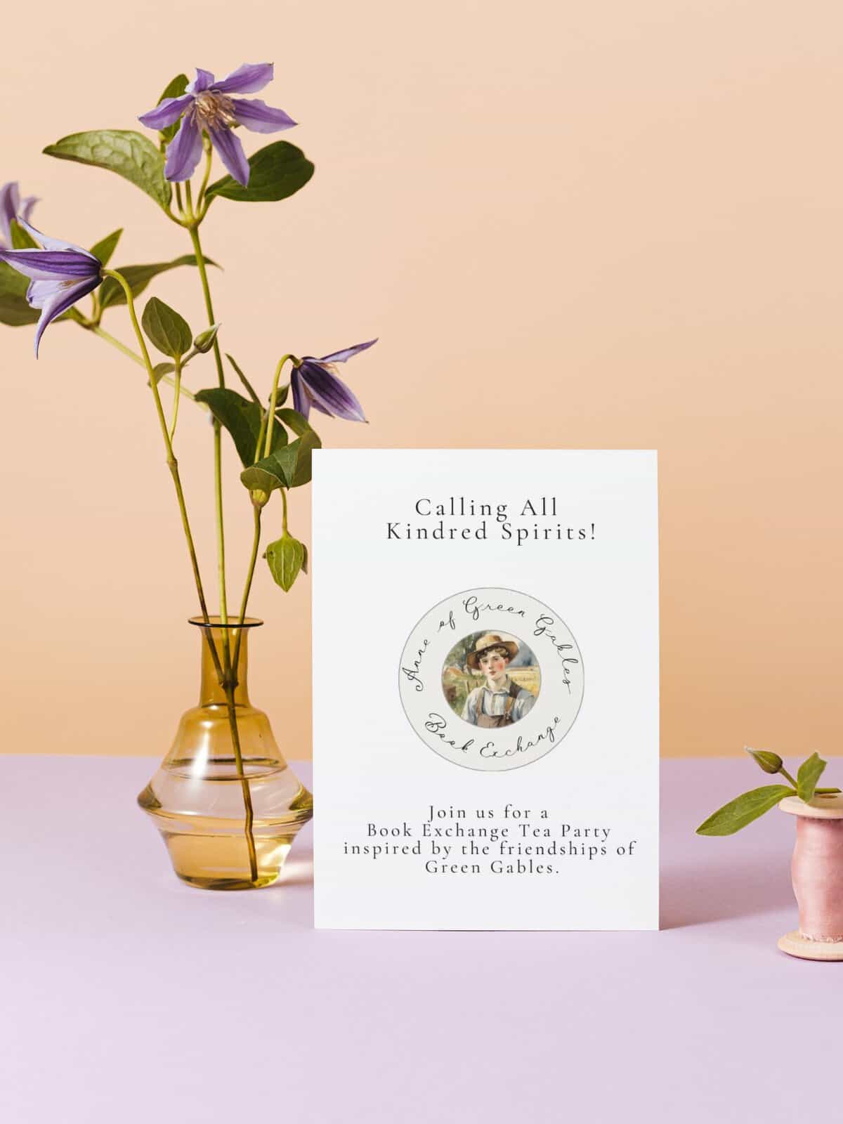 Gilbert Blythe book exchange invitation sitting next to a yellow vase with purple flowers.