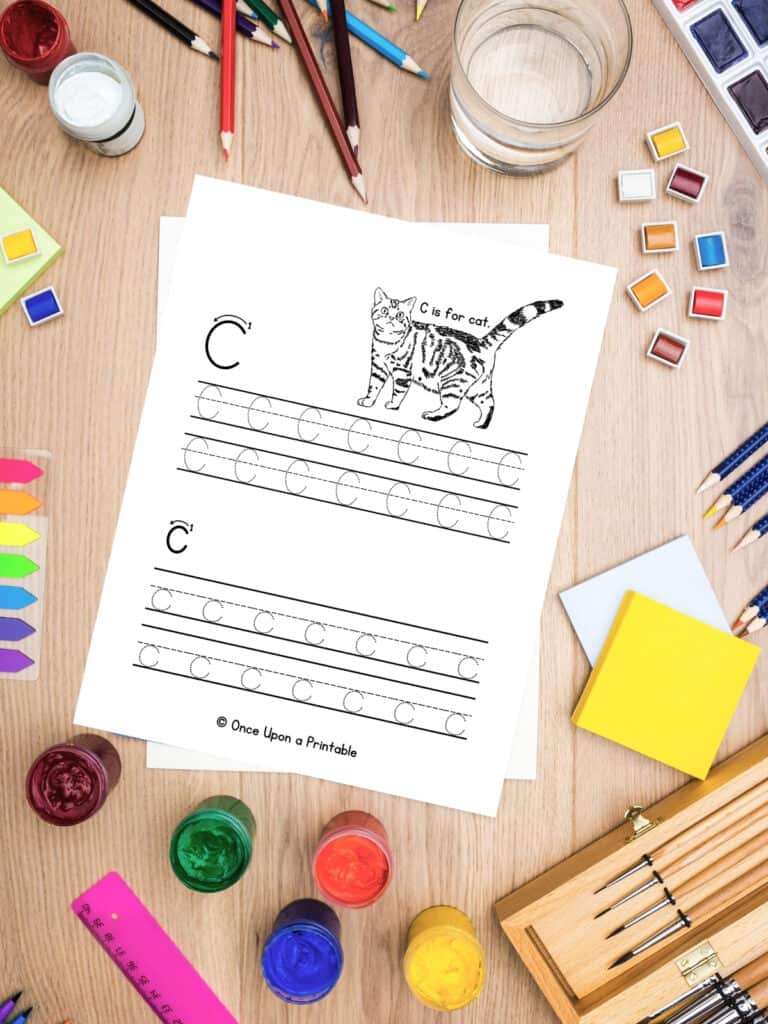 Letter C and lowercase c letter practice worksheet laying on a wooden table with coloring supplies.