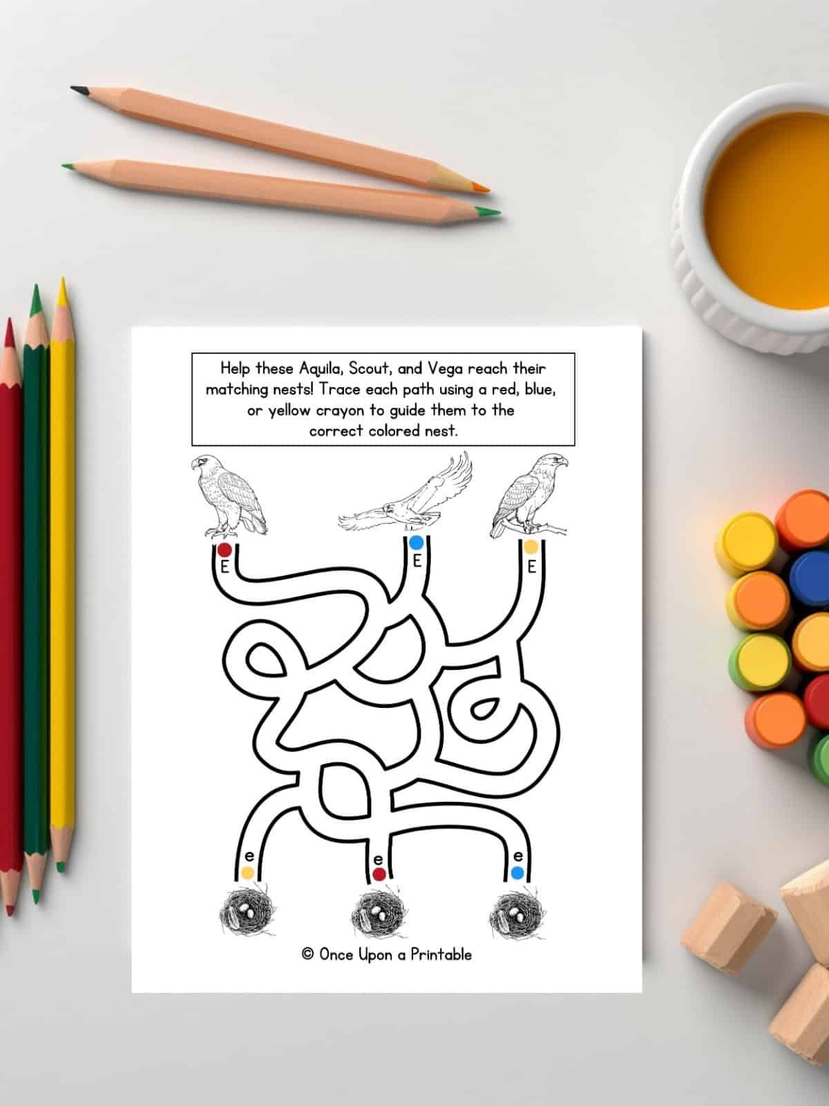 Letter E eagle, nest maze worksheet laying on a table with coloring pencils and paints.
