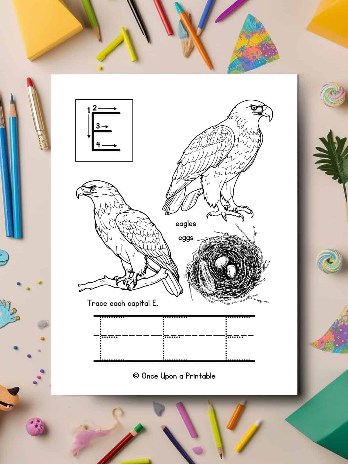 Letter E capital E tracing and coloring page with two eagles and a nest with eggs laying on a table with chaotic coloring pencils.