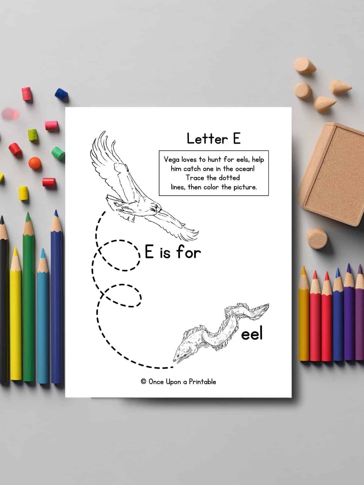 Letter E line tracing and coloring page laying on a table with coloring pencils.