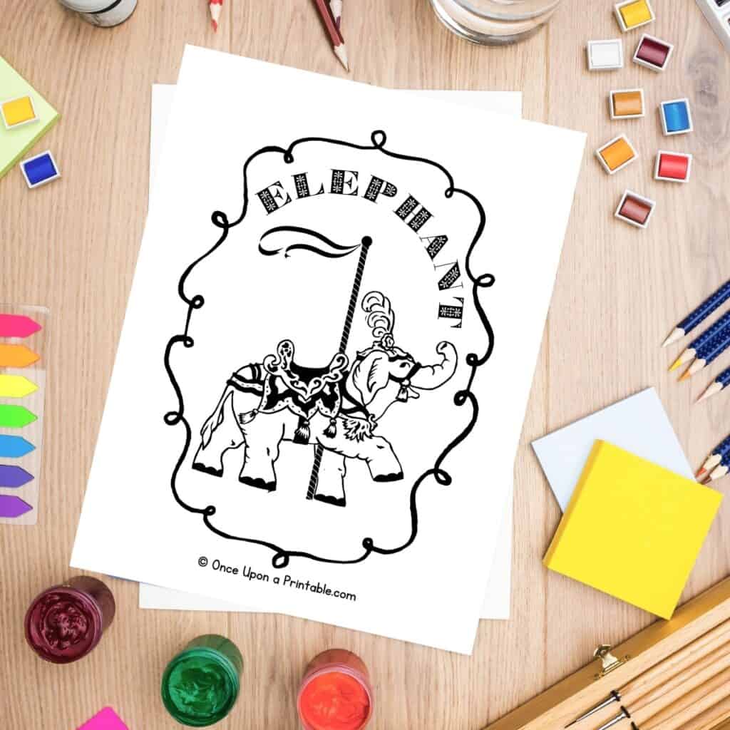 Zoo animal carousel coloring pages laying on a wooden table with coloring supplies like pencils and paints.