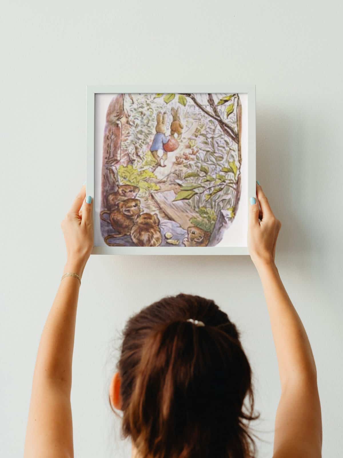 Benjamin Bunny illustrated wall art in a frame being held up by a woman's arms.