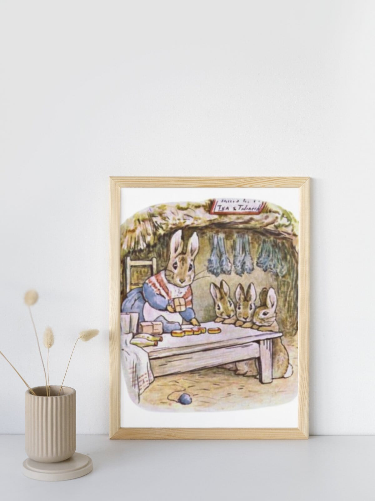 Mrs Rabbit with her little bunnies, illustration by Beatrix Potter framed and sitting on a table with a vase.