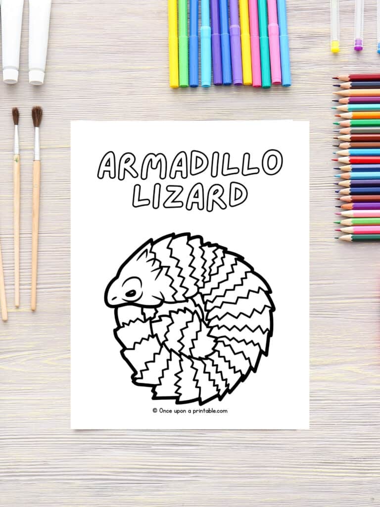 A is for Armadillo lizard animal coloring page laying on a wooden table with coloring pencils and paint brushes.