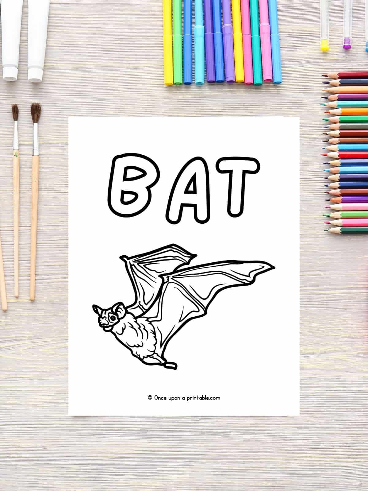 B is for Bat coloring page laying on a wooden table with coloring pencils.