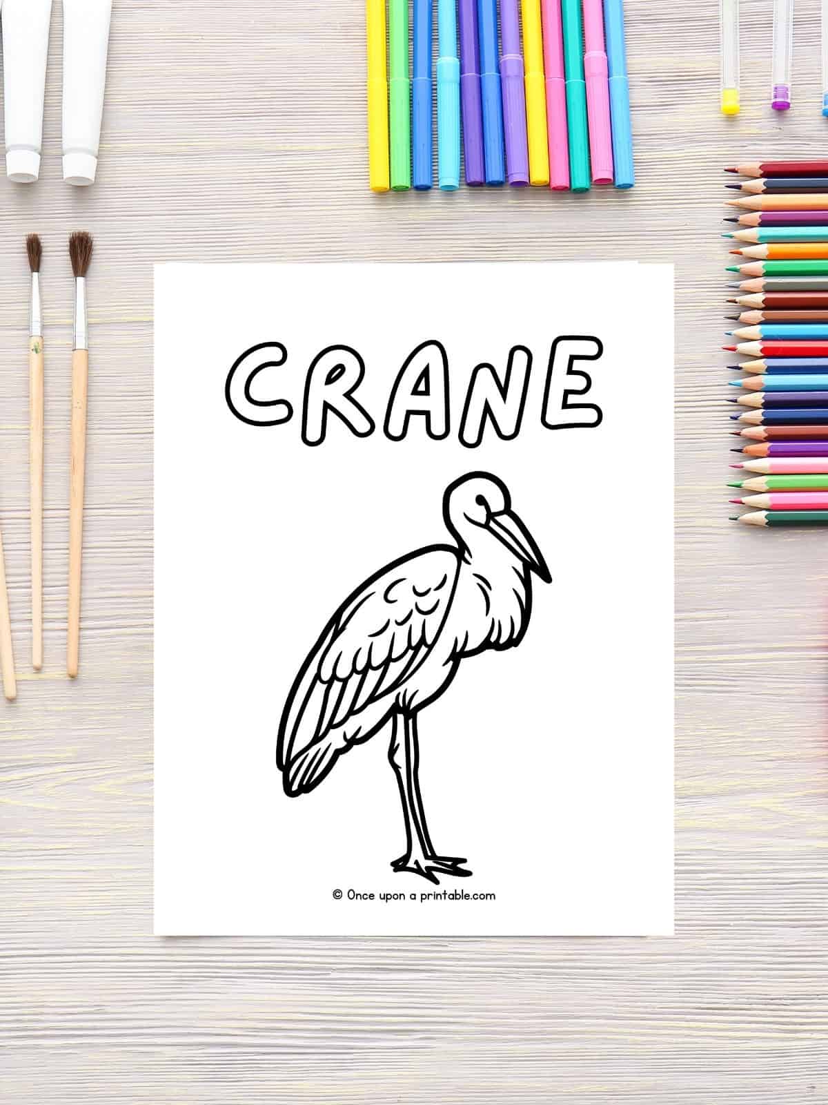 C is for Crane animal coloring page laying on a table with coloring supplies.