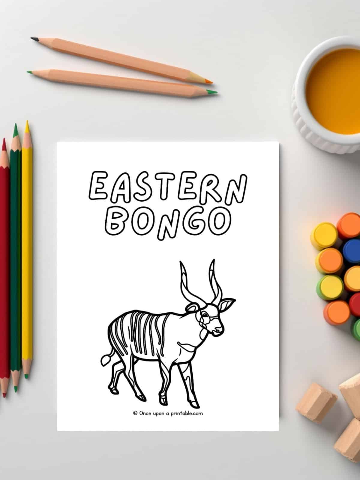 E is for Eastern Bongo coloring page of animal laying on a white table with paint and coloring pencils. 