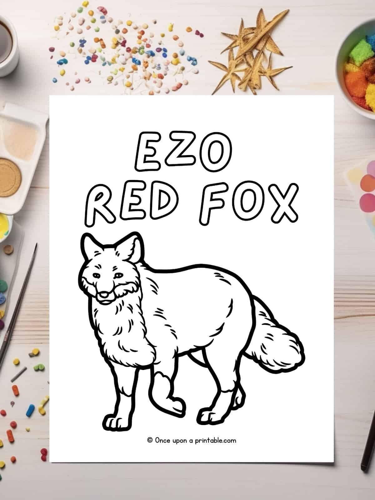 E is for Ezo red fox coloring page laying on a table with glitter. 