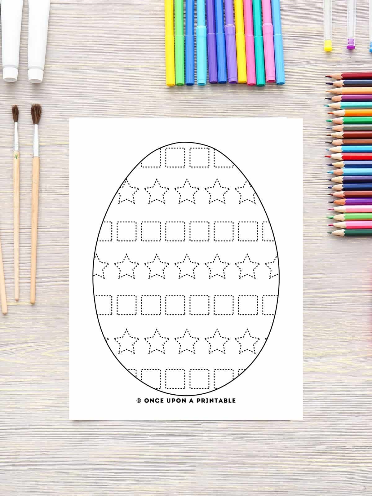 Egg tracing work page with stars and squares in a pattern laying on a wooden table with coloring pencils.