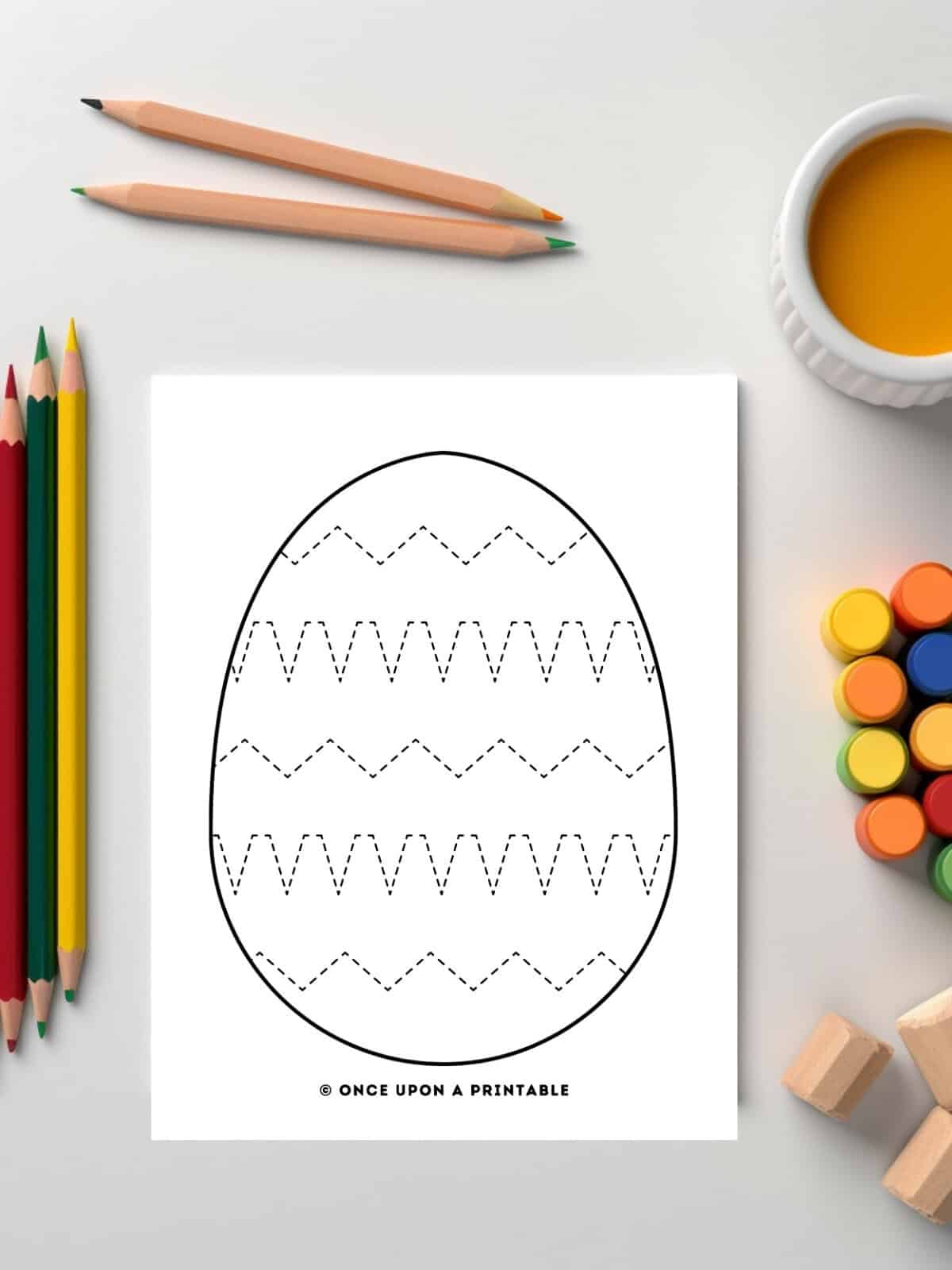 Easter egg tracing pages with zig zags laying on a table with coloring supplies.