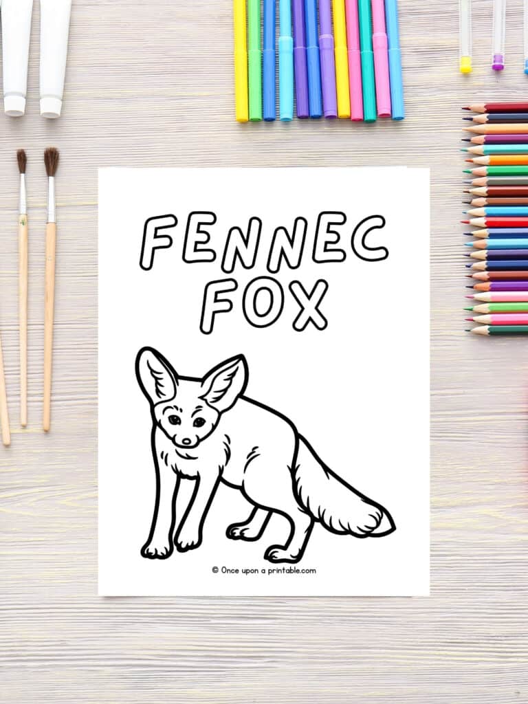 F is for Fennec Fox animal coloring page laying on a wooden table with coloring supplies. 