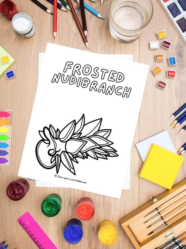 F is for Frosted Nudibranch animal coloring page on a table with coloring supplies. 