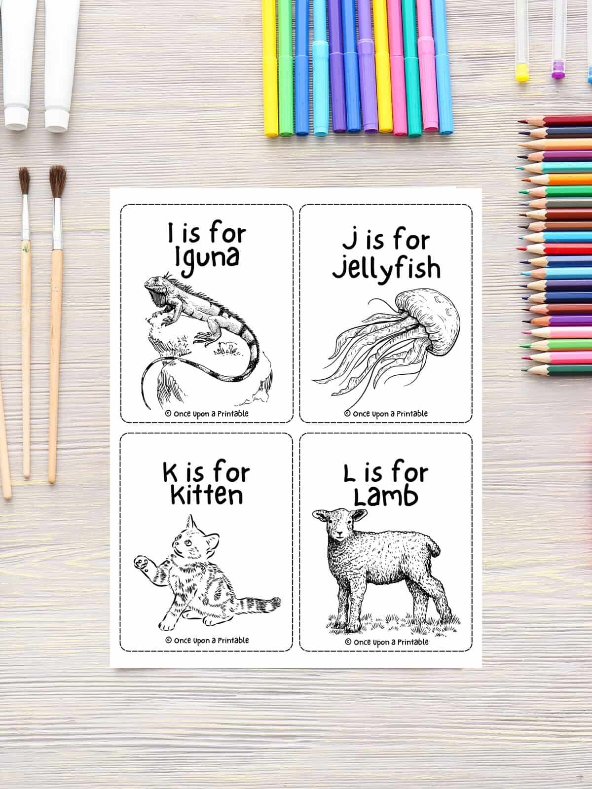 Flashcards for the alphabet with letters I through L coloring page laying on a wooden table with coloring pencils.