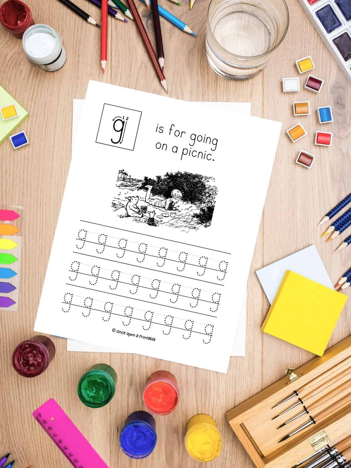 G is for going on a picnic classic Pooh tracing letter "g" worksheet laying on a table with lots of art supplies.