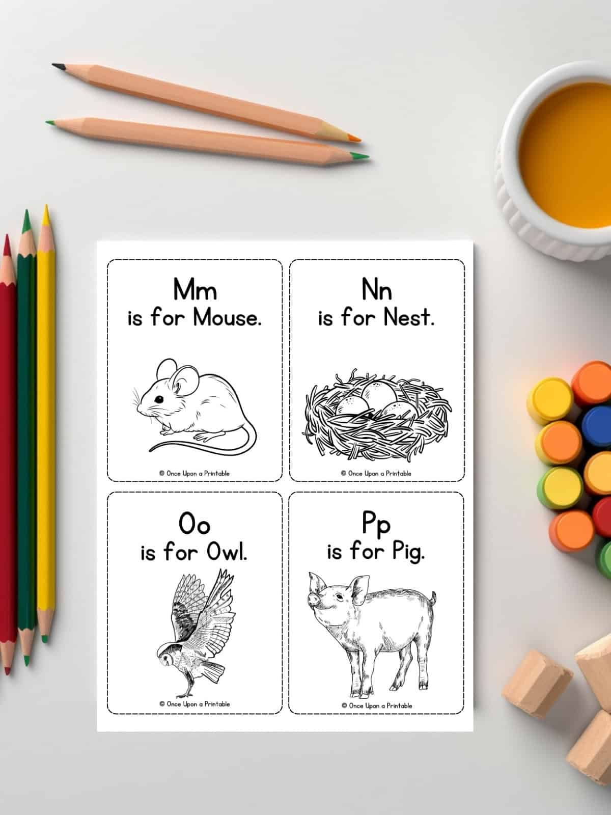 M-P coloring alphabet flashcards laying on a white table with coloring pencils and paint.