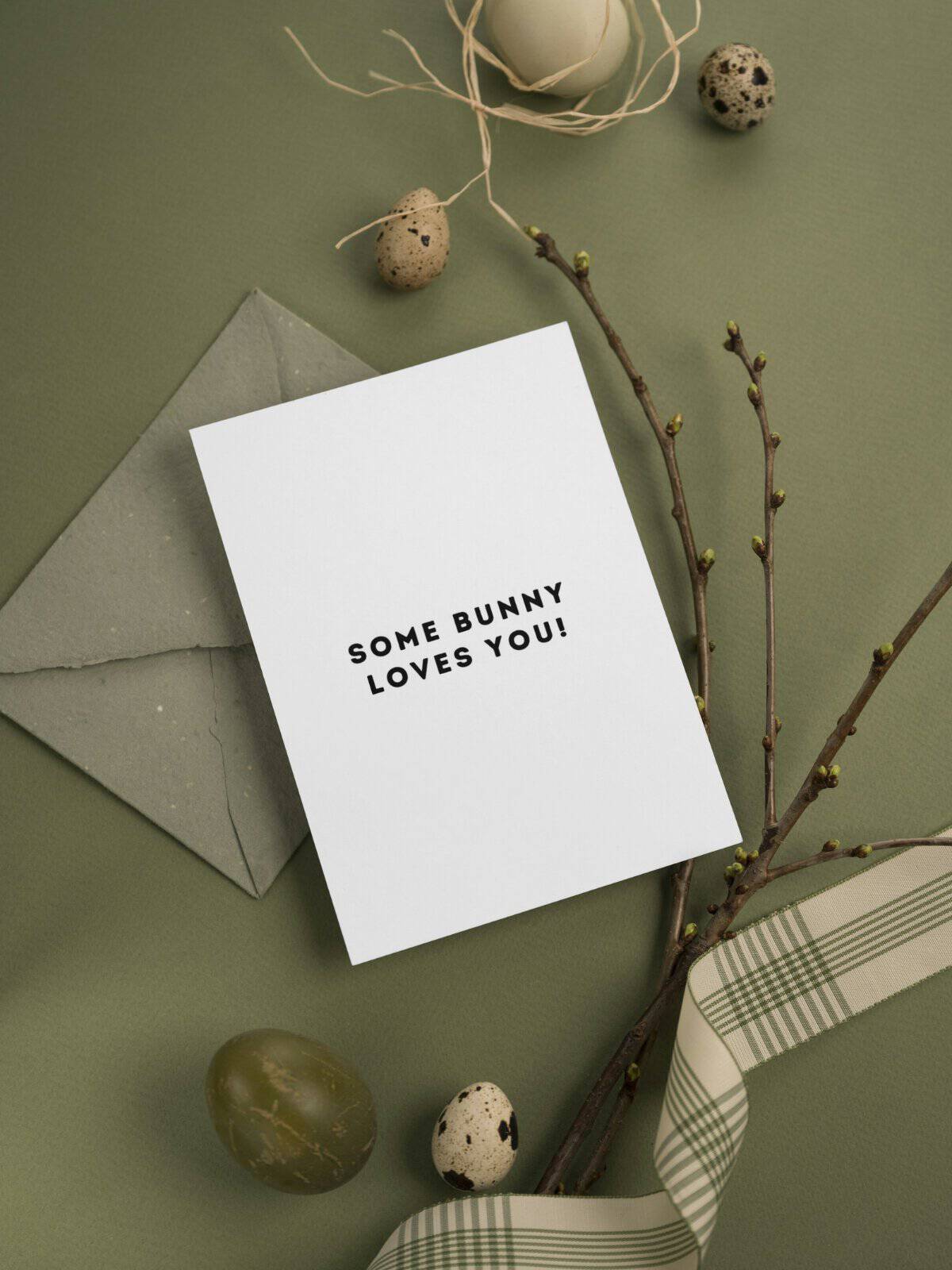 Some bunny loves you inside a Happy Easter card laying on a green backgound.