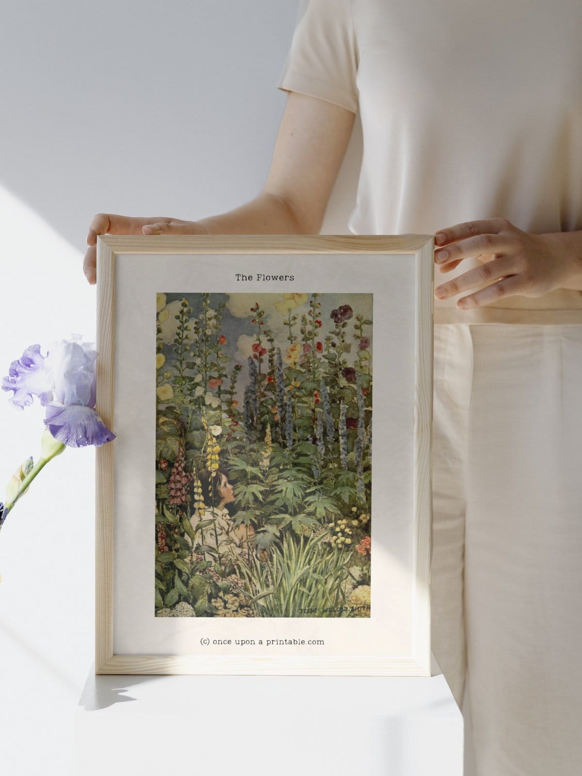 The Flowers illustrated colored art print by Jesse Willcox Smith framed and held by a woman. 