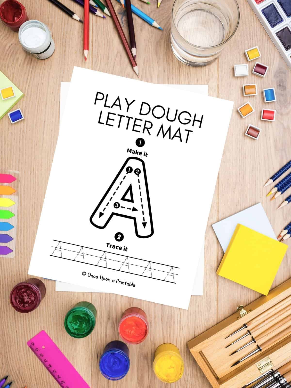 A tracing playdough mat laying on a table with art supplies.