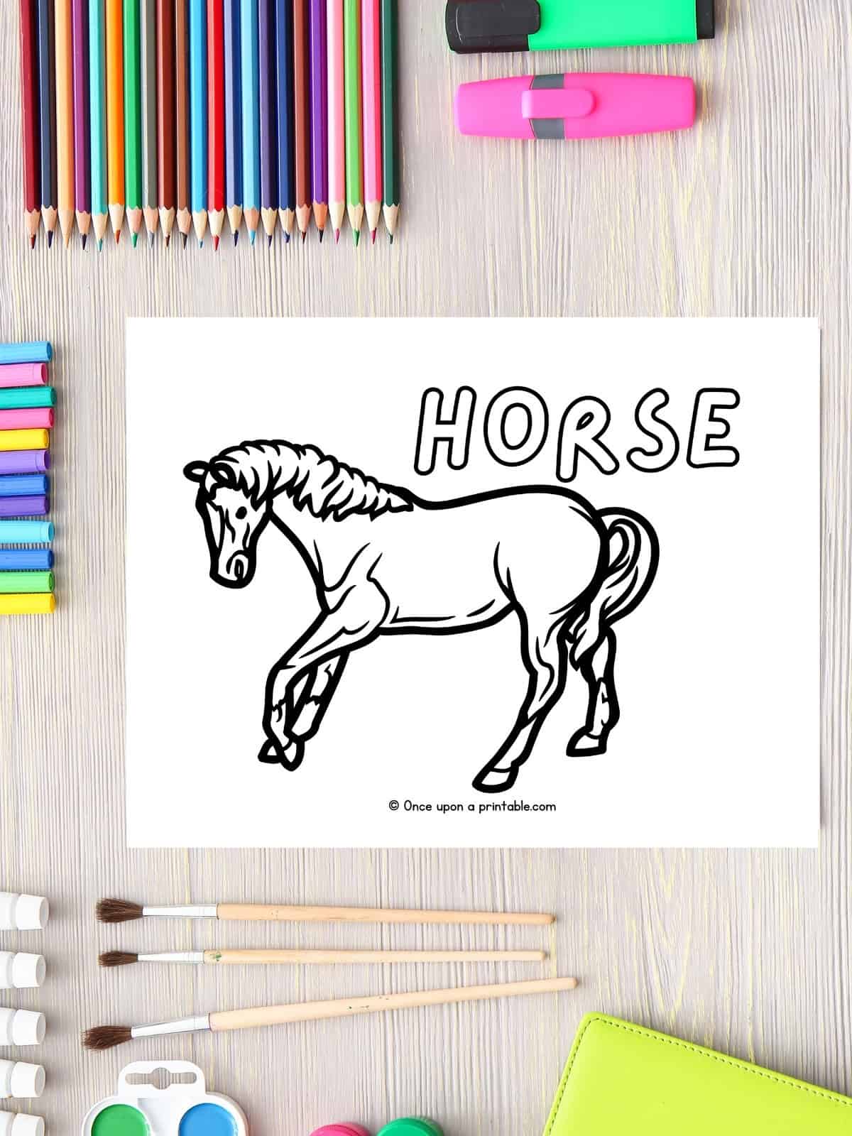 H is for Horse coloring page laying on a wooden table with coloring pencils and pain brushes. 