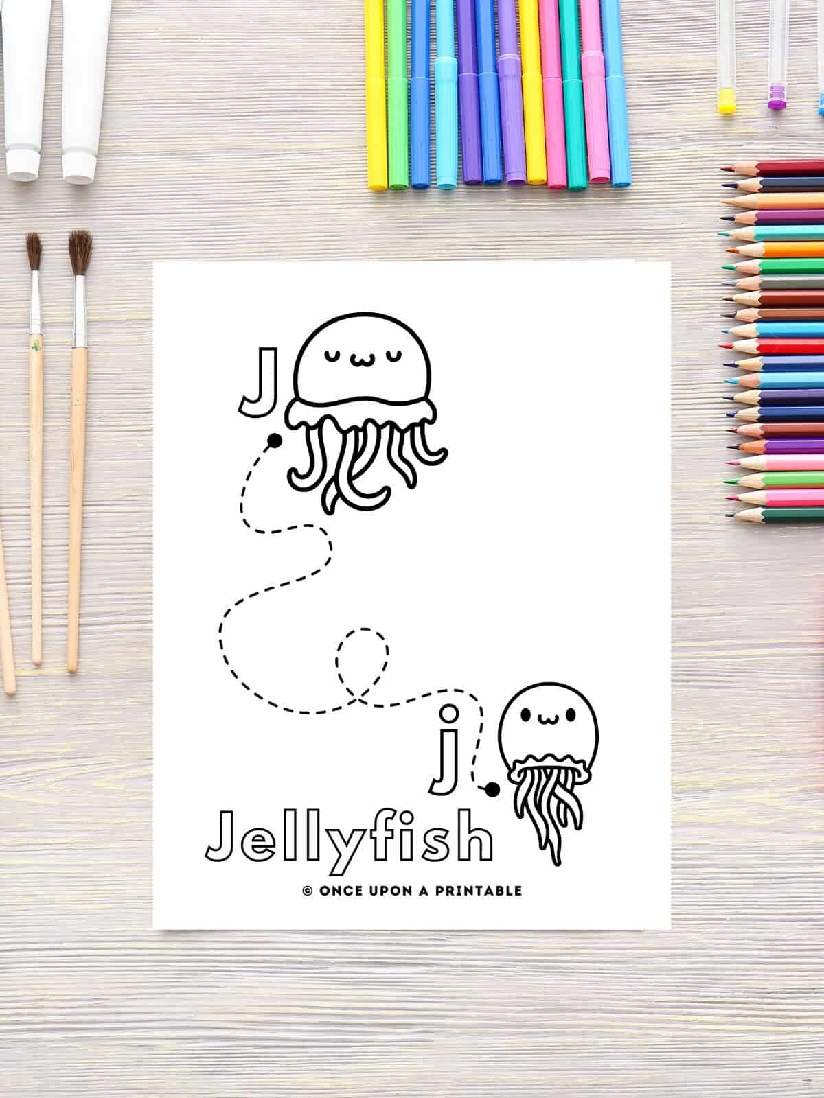 J is for Jellyfish line tracing coloring page for letter J laying on a table with color pencils.