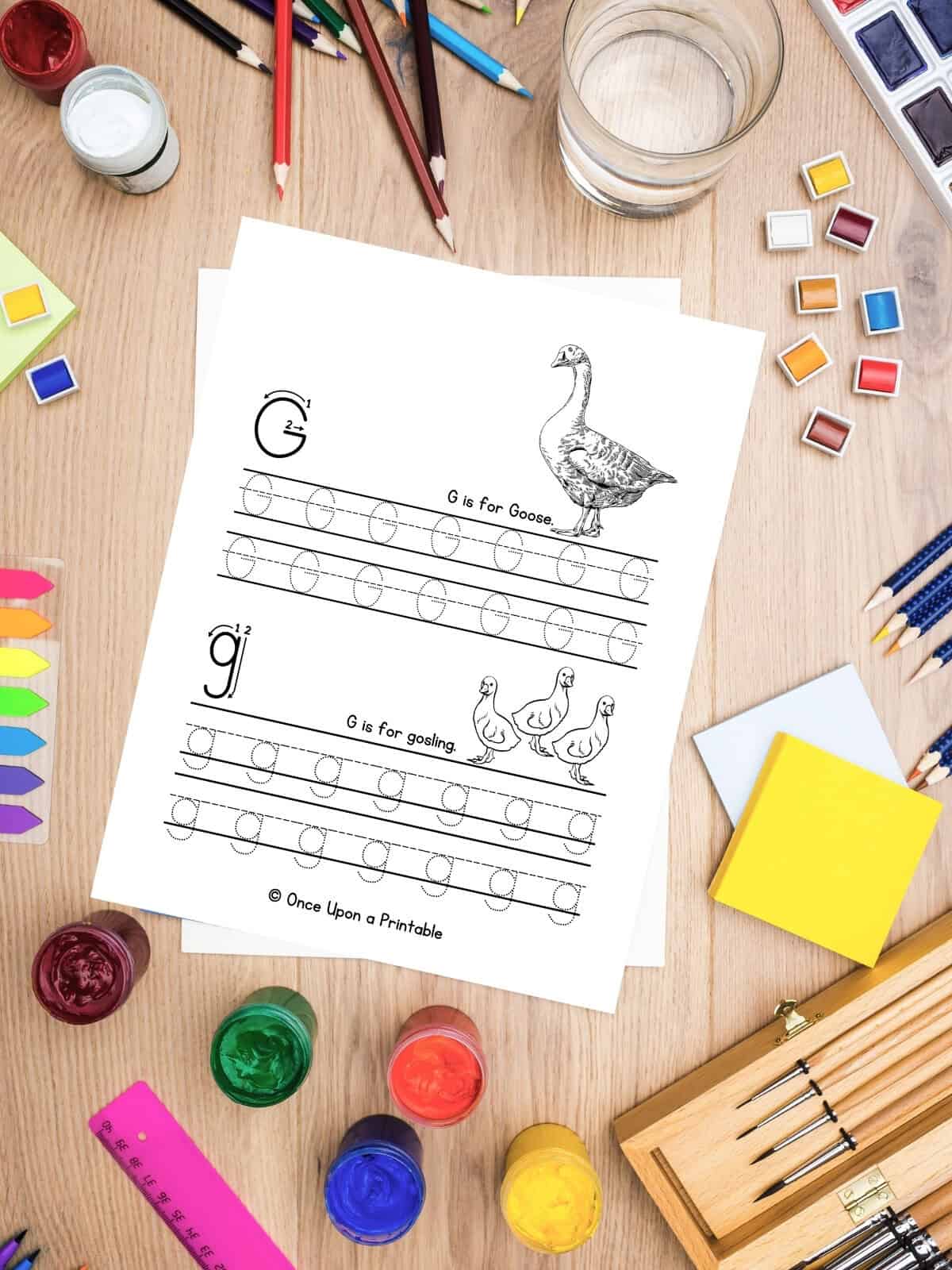 Letter G is for Goose letter practice sheets laying on a table and art supplies. 