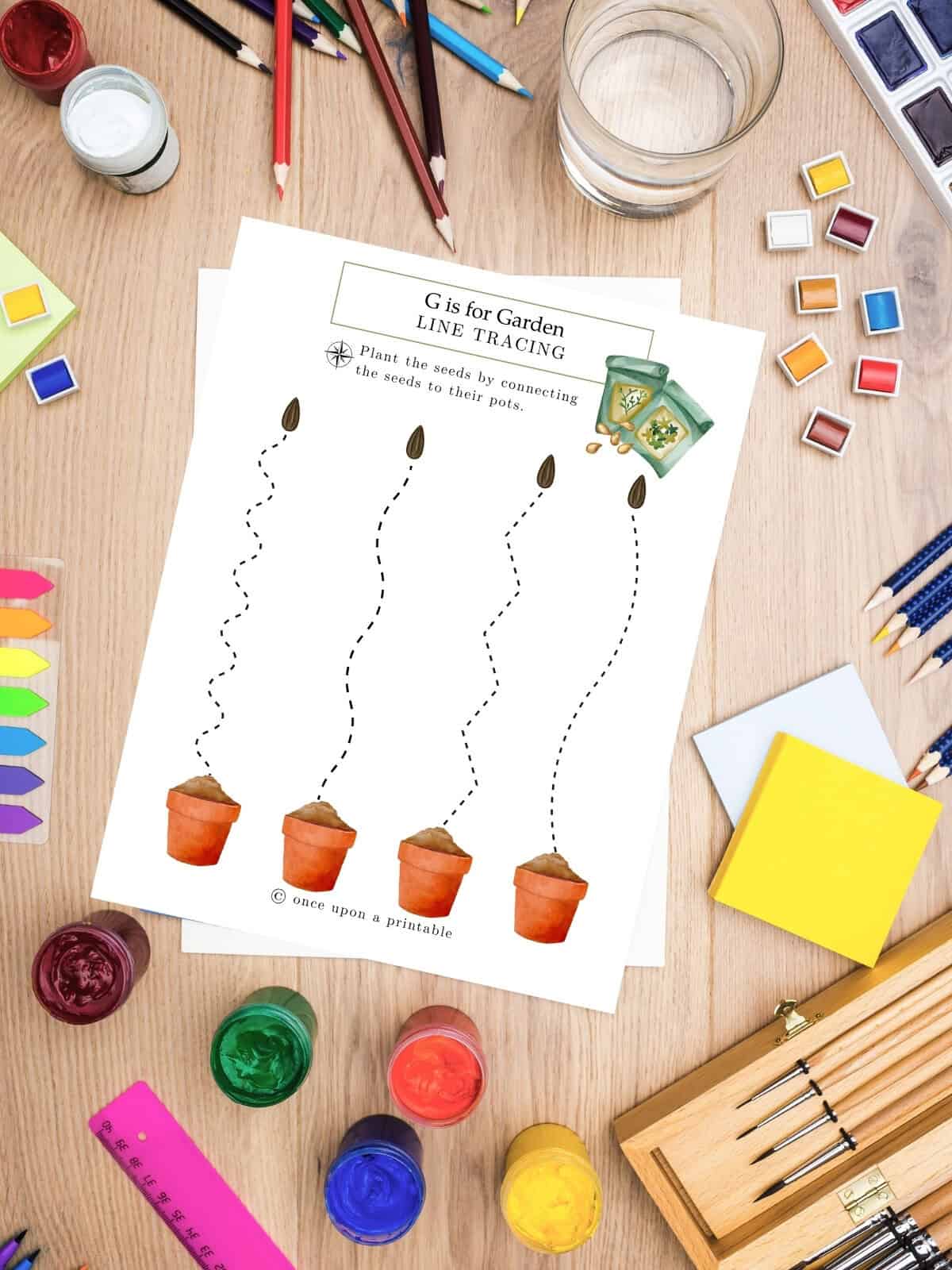 G is for garden line tracing activity page for preschool and kindergarten laying on a table with art supplies. 