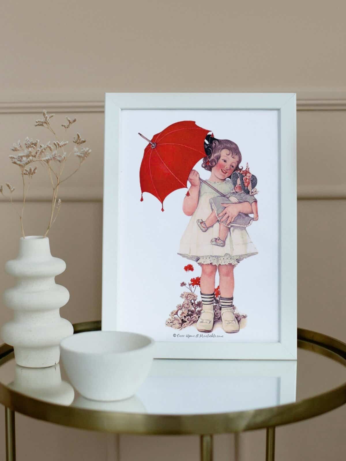 Sarah Stilwell Weber spring illustration of a little girl and her dolly under a red umbrella framed. 